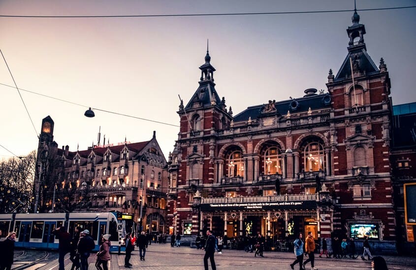 Leidseplein ao entardecer em Amsterdã, com edifícios históricos iluminados e pessoas passeando pela praça movimentada