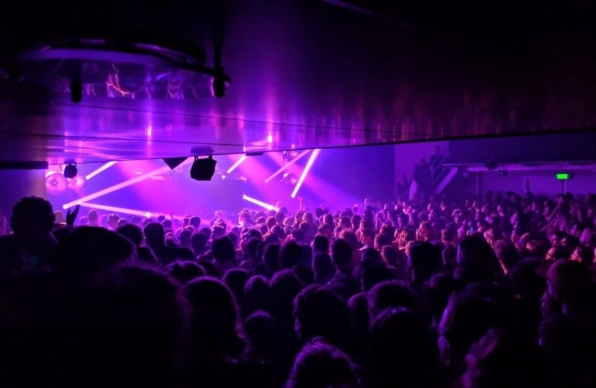 silhueta de multidão de pessoas em interior de balada, iluminada por luzes roxas