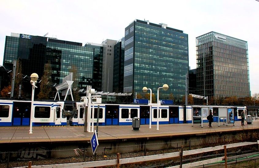 trem branco e azul parado em estação, em frente a prédios, durante o dia