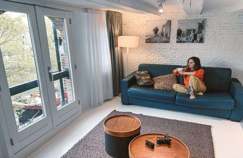 durante o dia, Bárbara Rocha tomando café em sofá de hotel com vista para a rua em Amsterdam