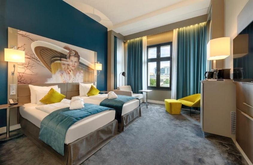 duas camas de solteiro, poltrona amarela e frigobar em suíte de um dos hotéis em berlim