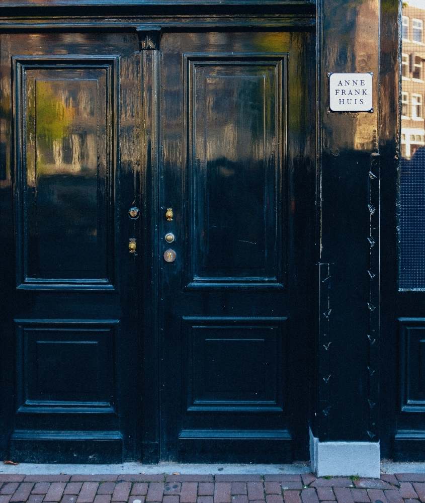 placa branca escrito 'anne frank huis' pendurada em grande porta preta de casa de anne frank, atração para quem busca o que fazer em Amsterdam