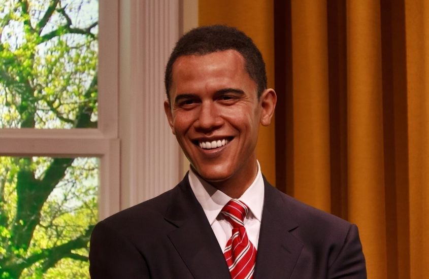 estátua de cera barack obama - ex presidente do estados unidos - sorrindo, com terno preto e gravata vermelha e branca
