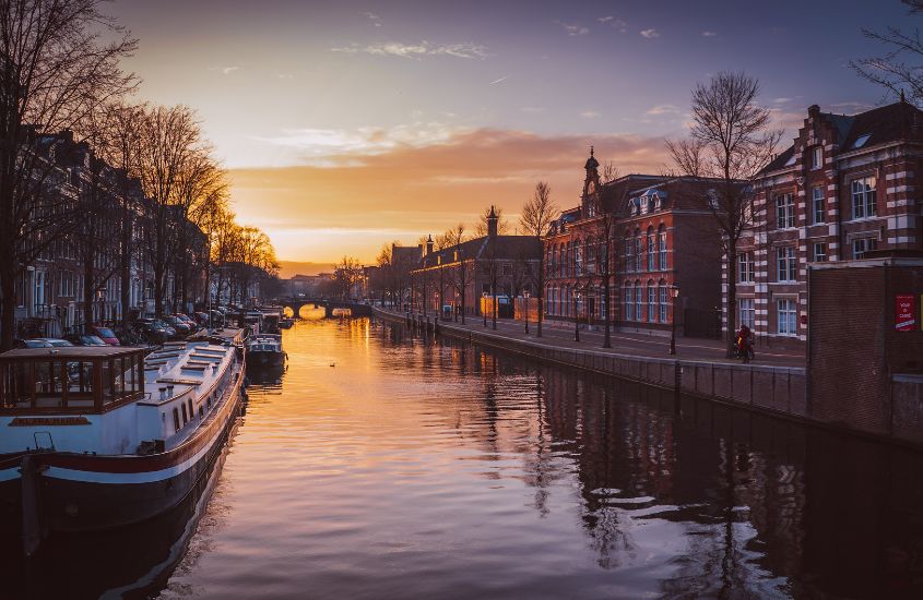durante entardecer, barcos em canal, atração imperdível ao fazer turismo em amsterdã