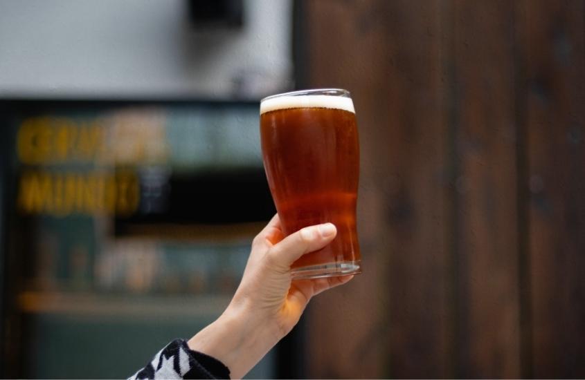 mão de mulher segurando copo cheia de cerveja para o alto, em bar, atração para quem busca o que fazer na guarda do embaú a noite
