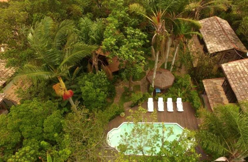 vista aérea de espreguiçadeiras, em frente a piscina cercada por árvores, durante o dia em um dos hotéis na guarda do embaú
