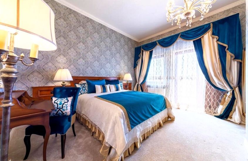 escrivaninha de madeira, poltrona azul e cama de casal em suite