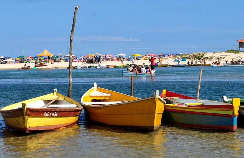 durante o dia, 3 banquinhos amarelos e vermelhos, atracados em mar de praia, lugar onde se hospedar na guarda do embaú
