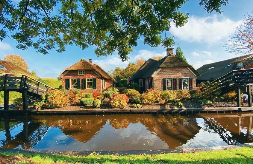 durante dia ensolarado, pequeno lago em frente a casa de tijolos vermelhos e telhado de palha em giethoorn, um dos melhores destinos holanda