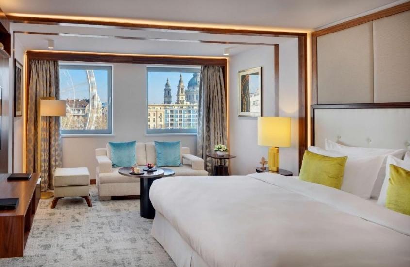 durante o dia, cama de casal e sofá brancos em suite com amplas janelas com vista para a cidade