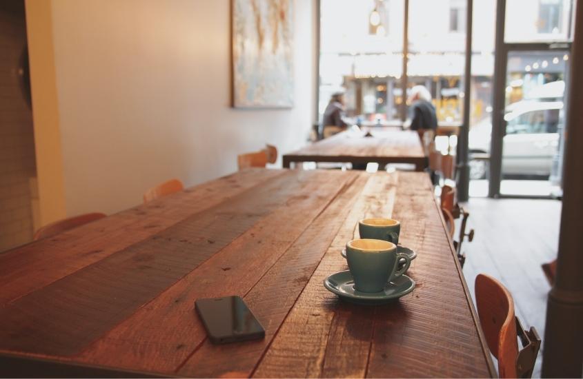 xícaras azuis e celular preto em cima de mesa de madeira em um café de bucareste romênia
