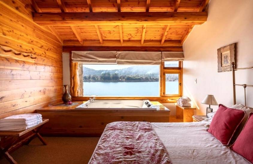 durante o dia, cama de casal e banheira de hidromassagem em suite com vista para o lago em uma das cabanas em bariloche