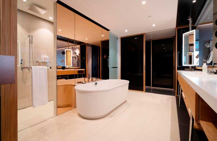 Interior de banheiro com banheira, chuveiro, toalhas, espelhos e móveis de madeira