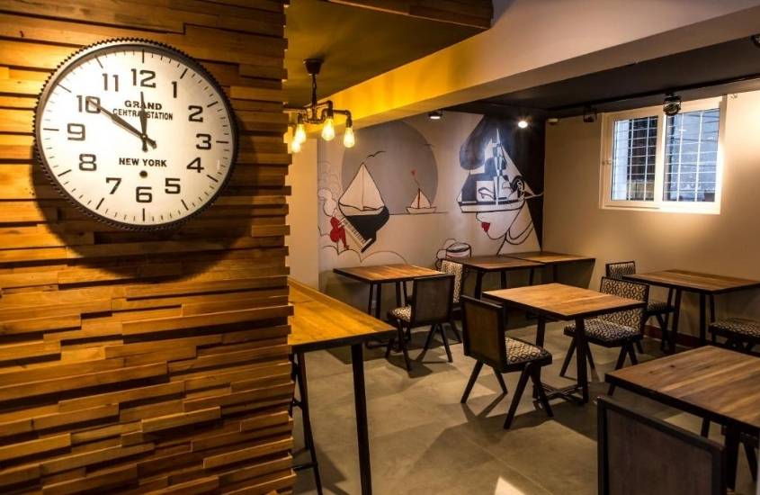 relógio de ponteiro pendurado em parede e ao fundo mesas e cadeiras em restaurante de um hostel em santiago do chile