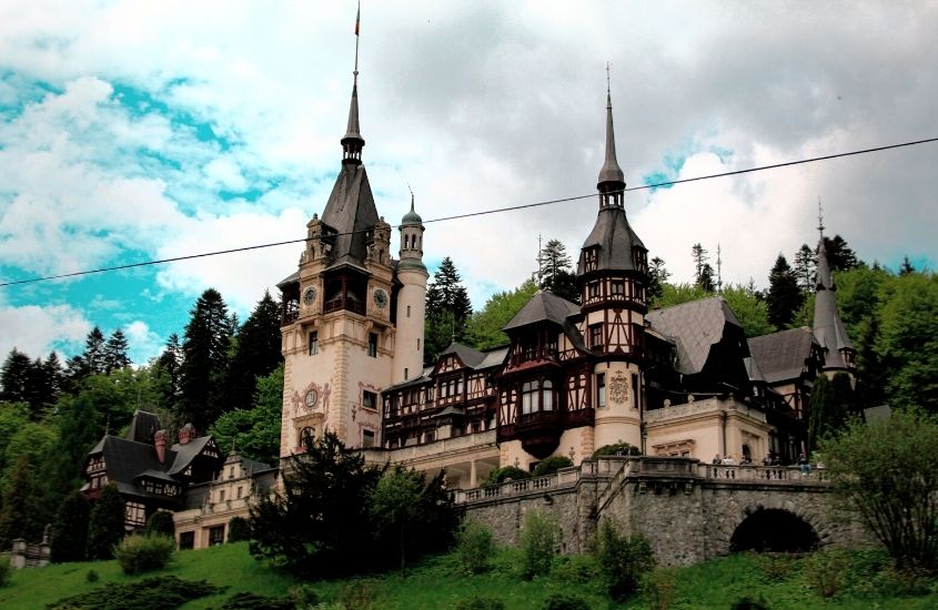 árvores ao redor de grande castelo, durante dia nublado em sinaia, destino para um roteiro romênia