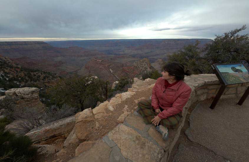 Durante o entardecer, Bárbara Alcantelado Rocha, criadora do blog melhores momentos da vida, no Gran Canyon com árvores ao redor