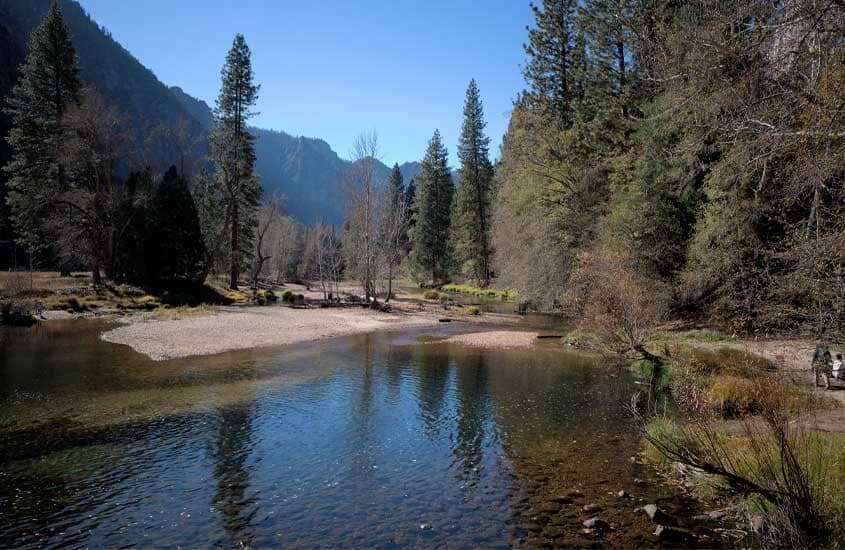 Em um dia de sol, Parque Nacional de Yosemite, um dos lugares para visitar nos Estados Unidos com árvores ao redor e lago na frente
