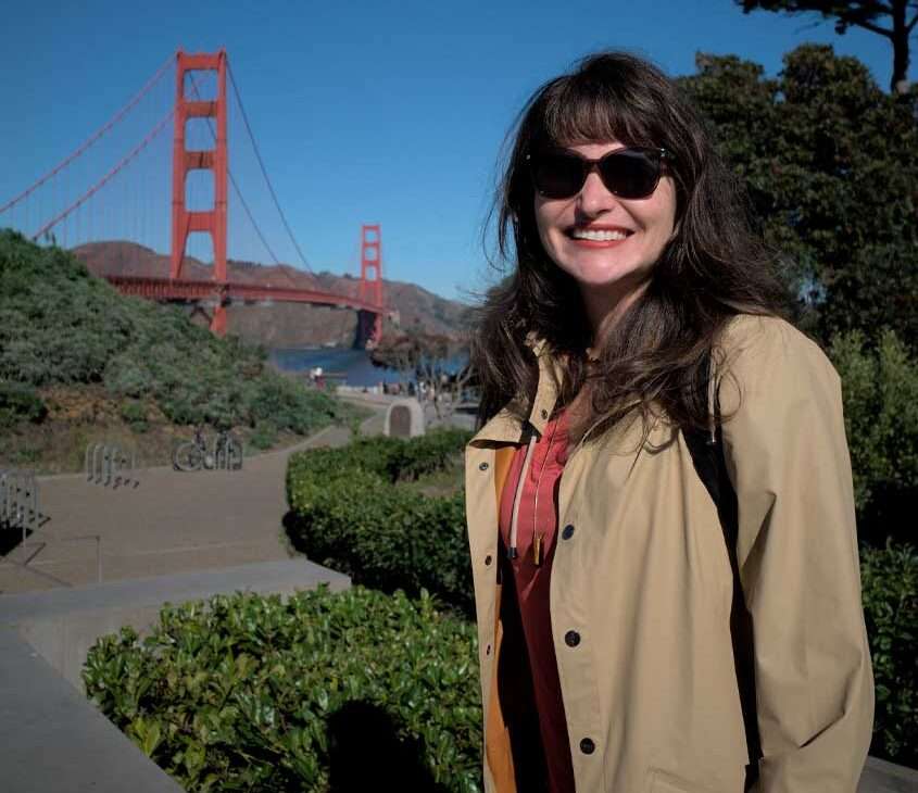 Em um dia de sol. Bárbara Alcantelado Rocha com árvores ao redor e Golden State Bridge atrás