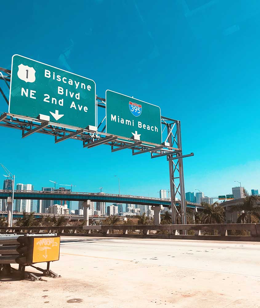 em avenida, duas placas de trânsito verdes, na da esquerda, há escrito 'biscayne blvd NE 2nd ave' e na da direita 'miami beach'