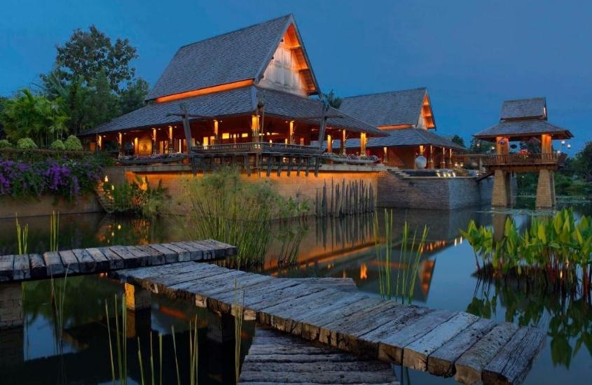 durante a noite, ponte de madeira sobre lago, e ao fundo, construção de madeira onde funciona um dos melhores resorts all inclusive do mundo