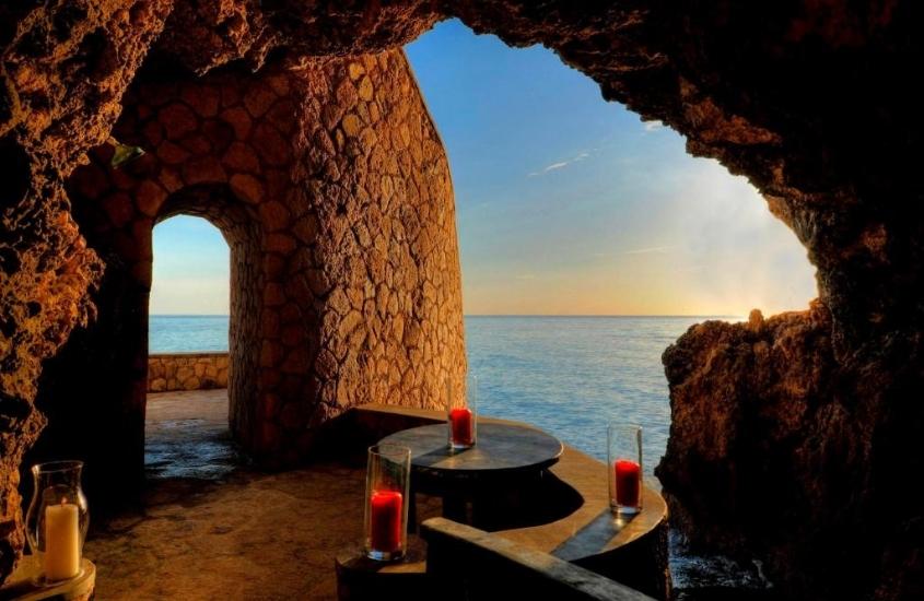durante a tarde, vela vermelha em cima de mesa redonda de madeira, dentro de caverna com vista para o mar