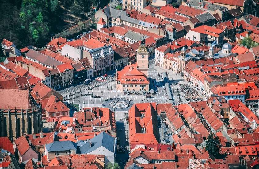 durante o dia, vista aérea de diversas casas com tijolos laranjas em centro histórico de brasov, um dos pontos turísticos da romenia