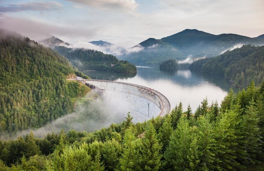 durante dia nublado, ponte ferroviária sobre lago, rodeada por montanhas verdes