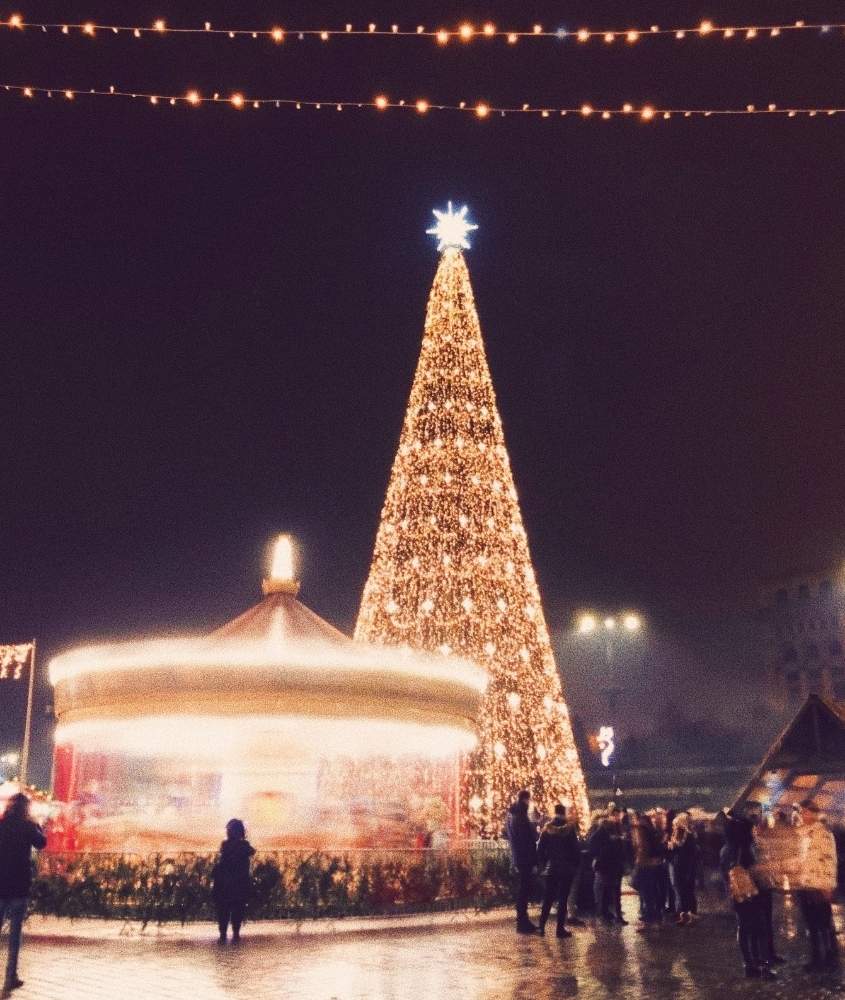 durante a noite, pessoas observando carrossel e árvore de natal iluminada
