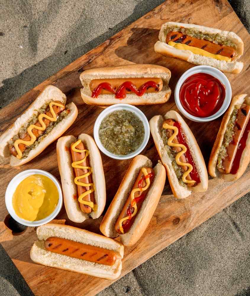 diversos hot dogs, cobertos com ketchup e mostarda, servidos em tábua de madeira