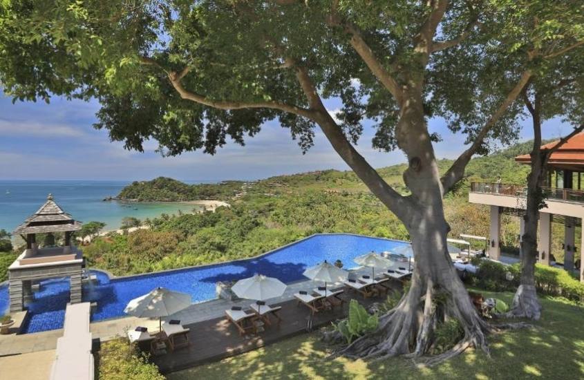durante o dia, grandes árvores em frente a piscina com vista para o mar em área externa de um resort na Tailândia