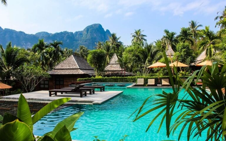 durante o dia, espreguiçadeiras ao redor de piscina, cercada por diversas árvores em um dos 25 resorts na Tailândia