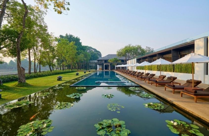 durante o dia, espreguiçadeiras em frente a piscina dentro de lago, em área de lazer externa de um dos hotéis de luxo na Tailândia