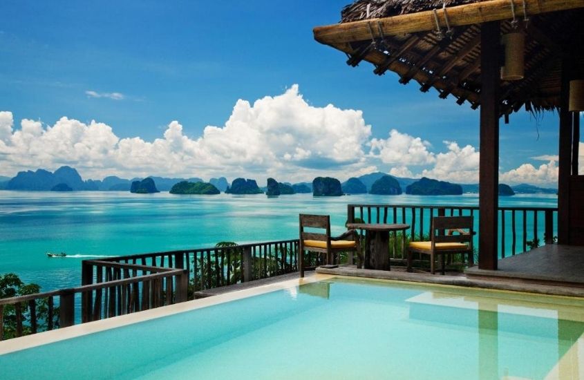 durante o dia, piscina e cadeiras de madeira em varanda com vista para o mar em um dos resorts na Tailândia