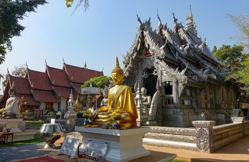 durante o dia, estátua dourada de buda sentado com as pernas cruzadas, e olhos fechados em frente a templos tailandeses