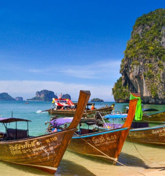 durante o dia, barcos de madeira com cauda longa, sobre o mar cristalino de uma das ilhas para turismo na tailândia
