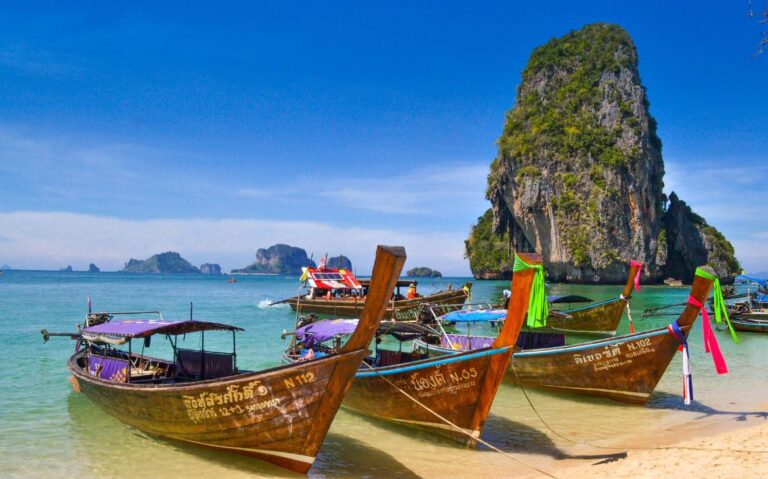 durante o dia, barcos de madeira com cauda longa, sobre o mar cristalino de uma das ilhas para turismo na tailândia