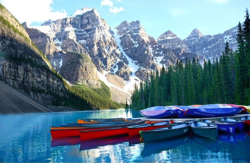 durante o dia, canoas vermelhas e azuis em lago azul, ao fundo, picos nevados