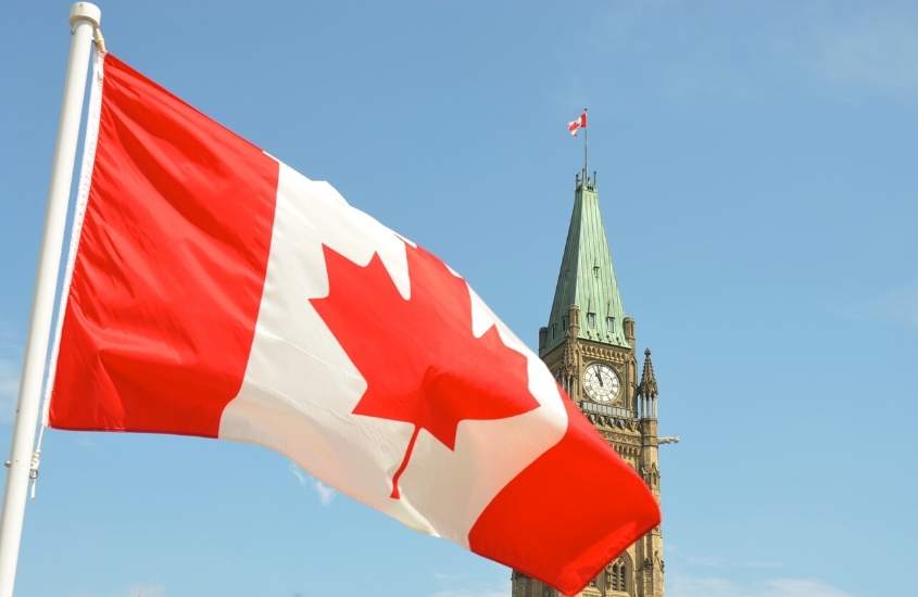 durante o dia, bandeira do canadá hasteada, ao fundo, torre com telhado verde