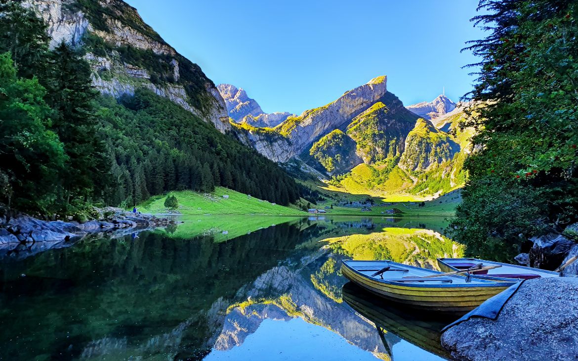 durante o dia, duas canoas em lago e, ao fundo, montanhas iluminadas pelo sol