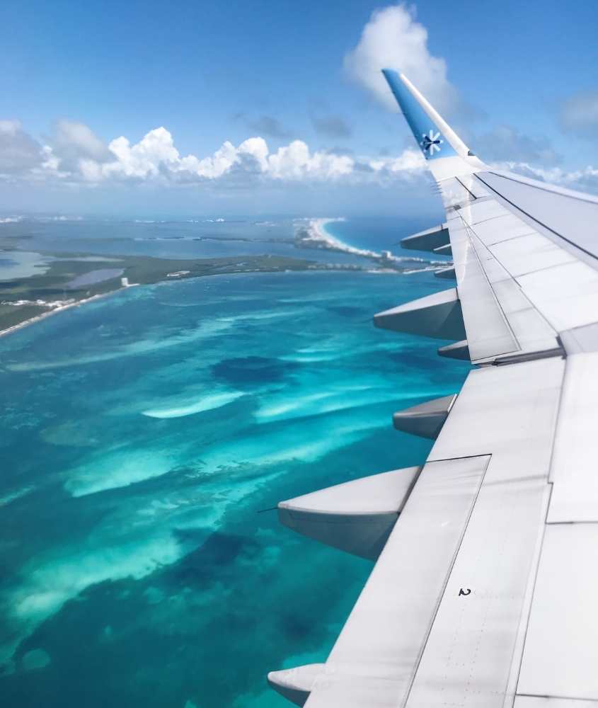 durante o dia, asa de avião passando sobre o mar em viagem para cancún