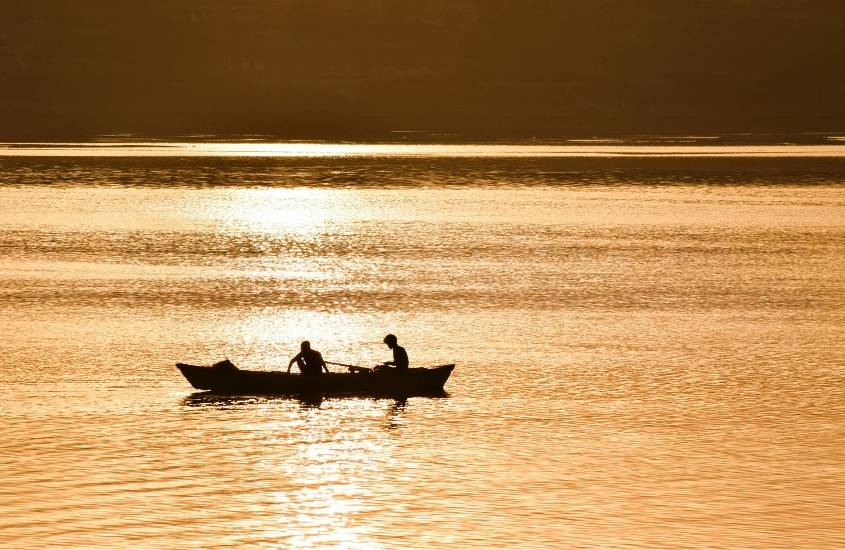 durante o dia, silhueta de duas pessoas em canoa sobre o rio ganges, ponto turístico da Índia