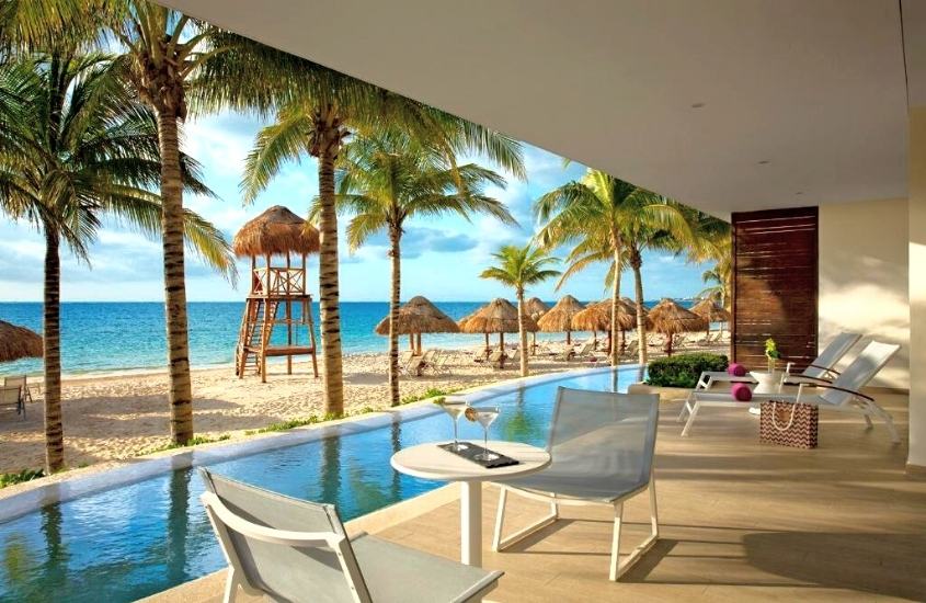 durante o dia, cadeiras, mesa e espreguiçadeiras em frente a piscina com vista para a praia em um dos melhores hotéis em Cancún