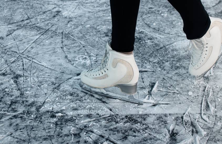 pernas de pessoa com calça preta e patins brancos, patinando em pista de gelo, atração para quem busca o que fazer no parque yosemite no inverno