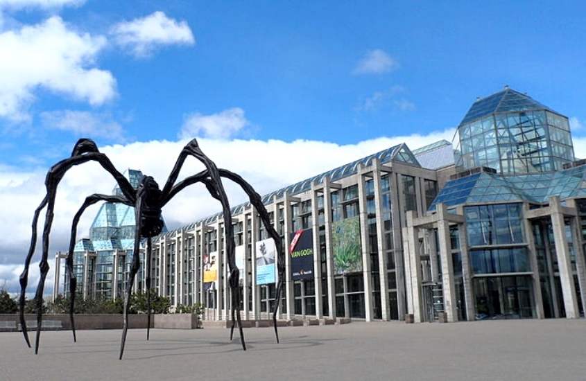 durante o dia, escultura em formato de aranha em frente a prédio com estrutura de vidro