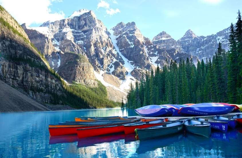 durante o dia, canoas vermelhas, azuis e verdes em lago cercado por árvores e montanhas