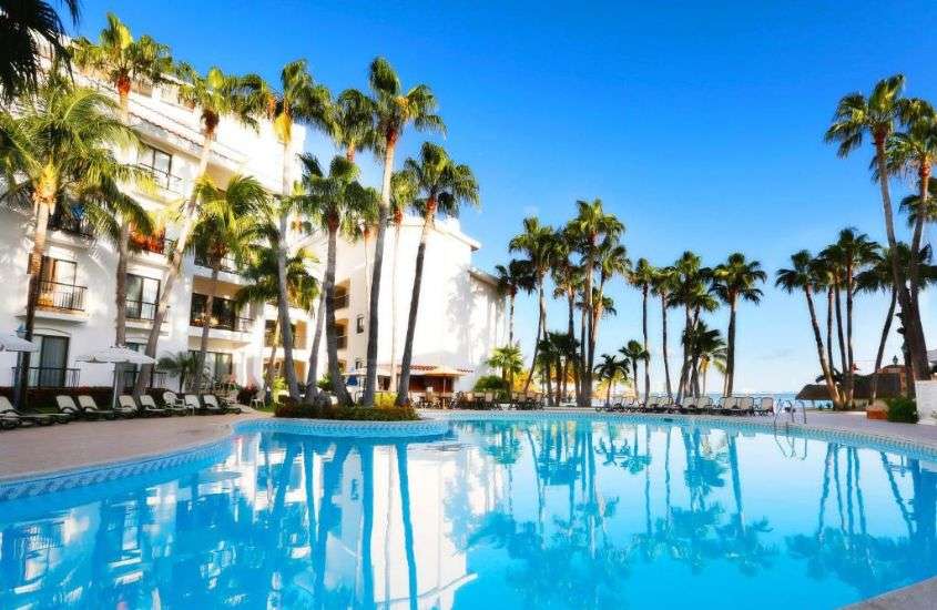 durante o dia, coqueiros e espreguiçadeiras ao redor de piscina em um dos melhores hoteis em cancun