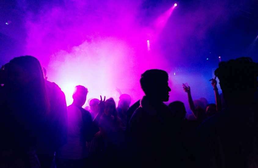 silhueta de pessoas dançando em balada iluminada por luzes roxas