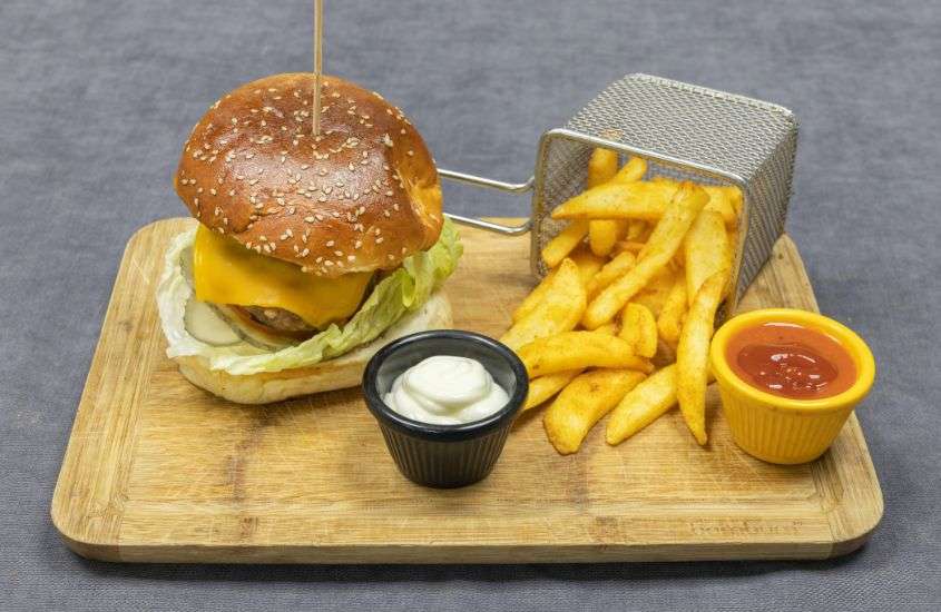 hambúrguer, batata frita e potes de ketchup e maionese em cima de tábua de madeira