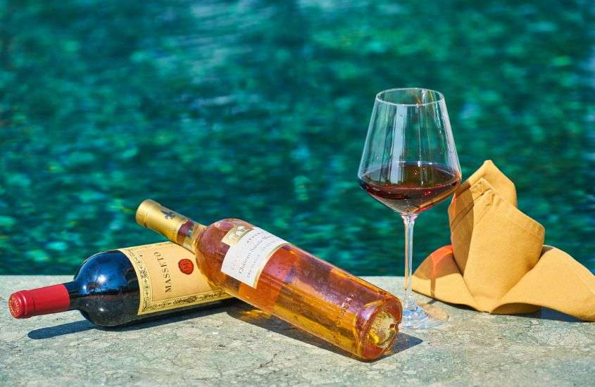 durante o dia, garrafas e taça de vinho em frente a piscina