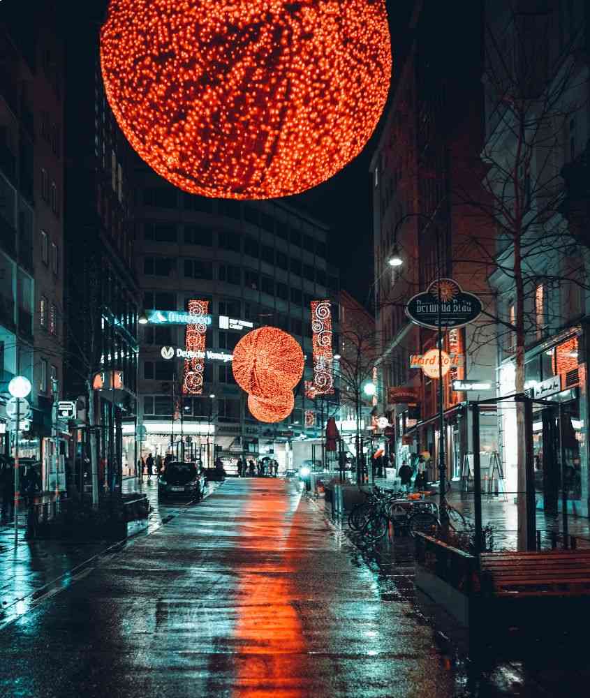 durante a noite, carros, bicicletas e pessoas em rua decorada com bolas vermelhas iluminadas